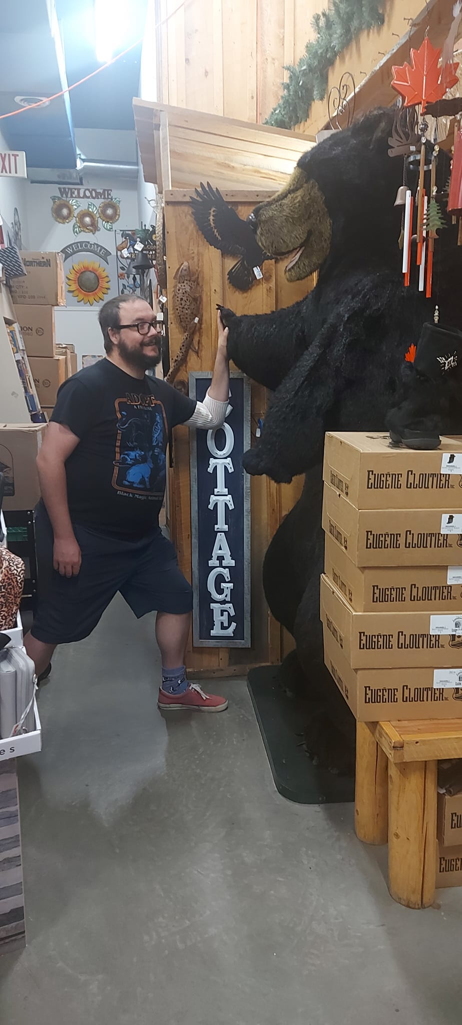 A man short hair and bushy facial hair high fives a large fluffy black bear statue